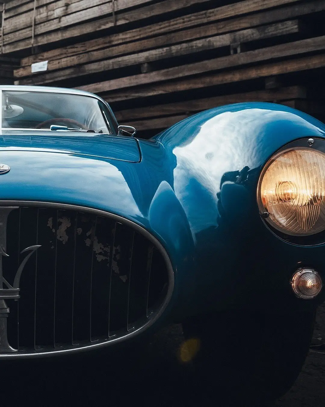 نمای جلویی و جانبی خودروی کلاسیک مازراتی A6GCS فارینا برلینتا به رنگ آبی متالیک با رینگ‌های پره‌ای در مقابل یک بنای سنتی اروپایی.