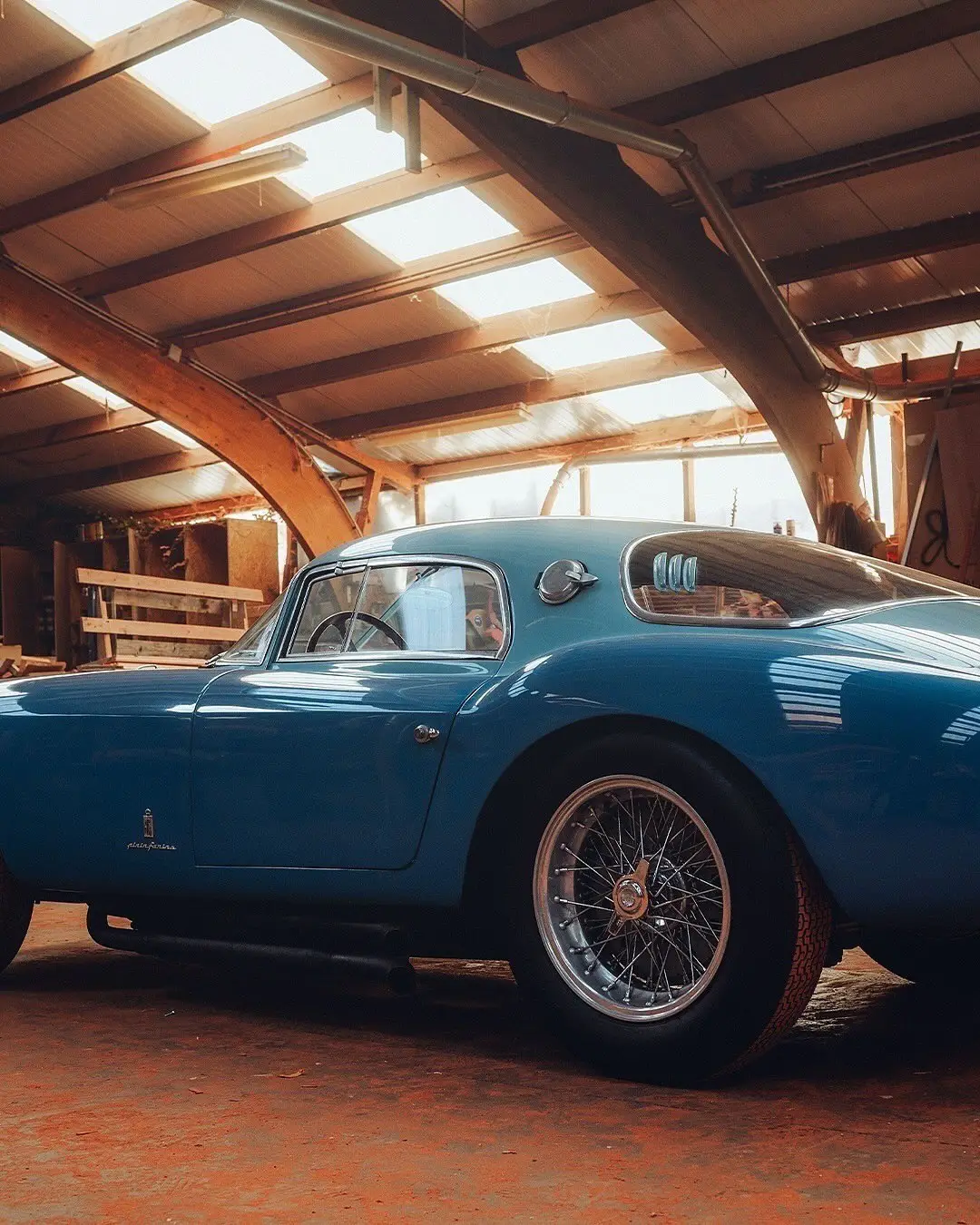 نمای جلویی و جانبی خودروی کلاسیک مازراتی A6GCS فارینا برلینتا به رنگ آبی متالیک با رینگ‌های پره‌ای در مقابل یک بنای سنتی اروپایی.