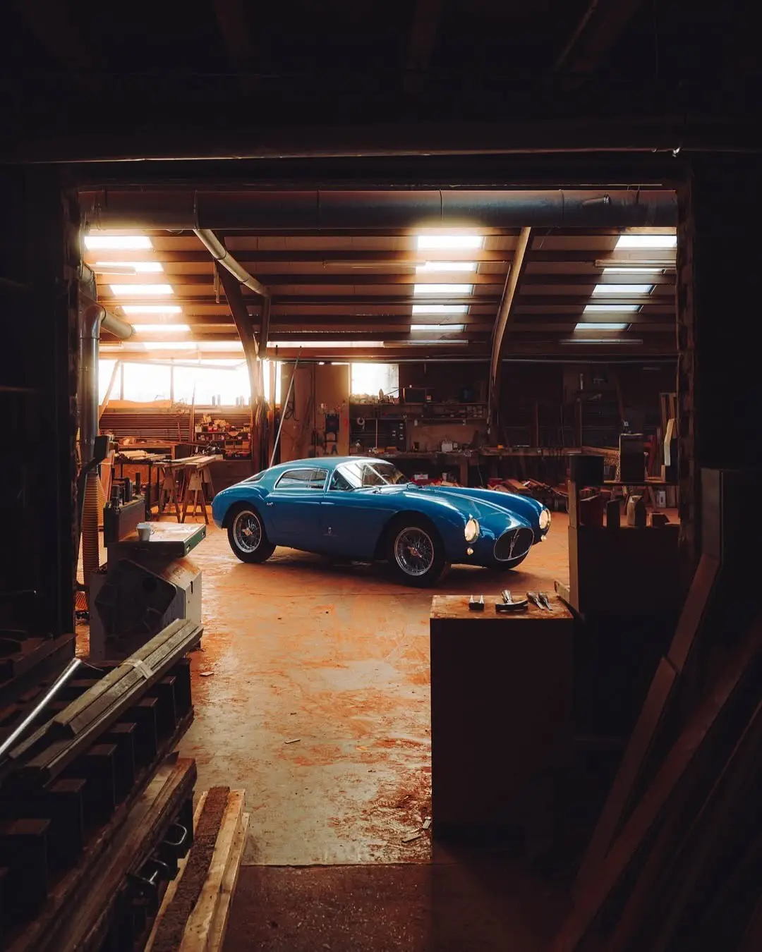 نمای جلویی و جانبی خودروی کلاسیک مازراتی A6GCS فارینا برلینتا به رنگ آبی متالیک با رینگ‌های پره‌ای در مقابل یک بنای سنتی اروپایی.