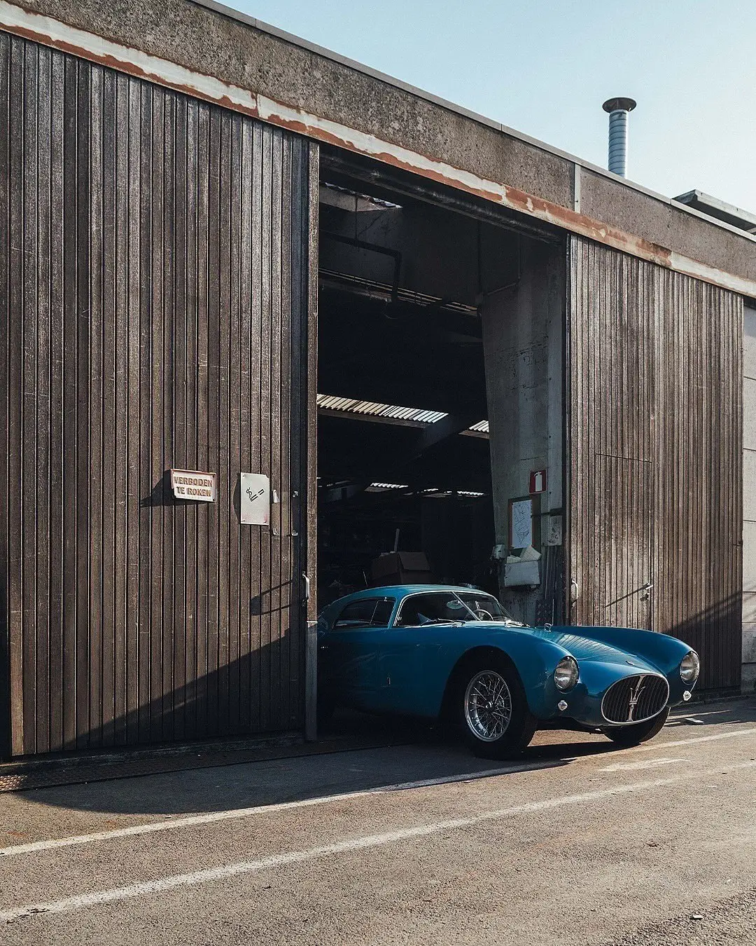 نمای جلویی و جانبی خودروی کلاسیک مازراتی A6GCS فارینا برلینتا به رنگ آبی متالیک با رینگ‌های پره‌ای در مقابل یک بنای سنتی اروپایی.