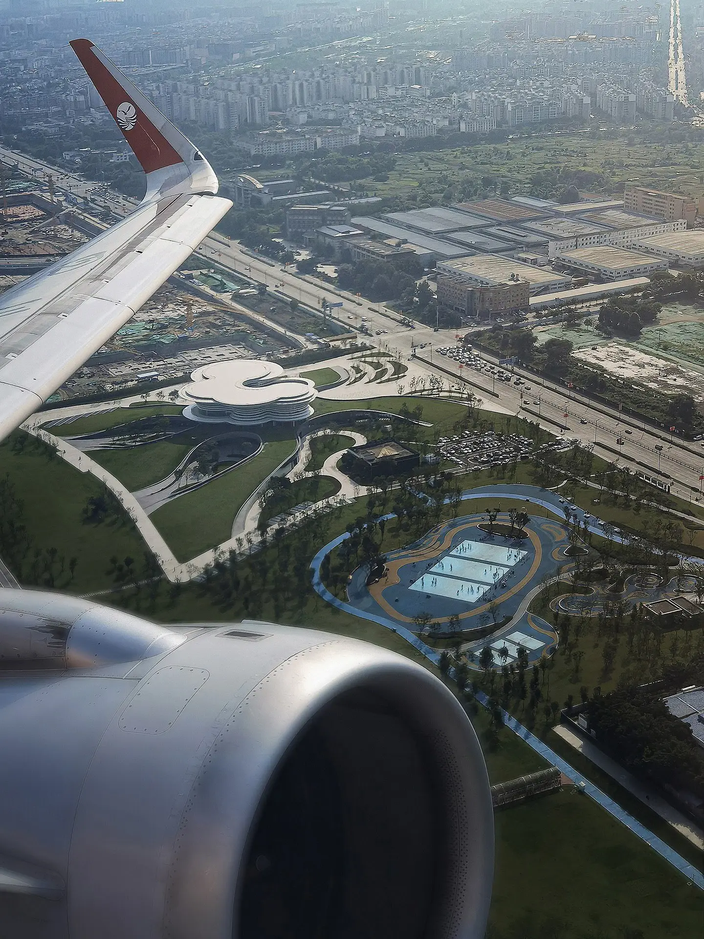 نمای ساختمان مدرن و معلق مرکز نمایشگاهی ابر فرودگاه چنگدو با طراحی سفید و کشیده بر فراز فضای سبز که نشان‌دهنده سبک معماری انتزاعی شرکت CSWADI است.