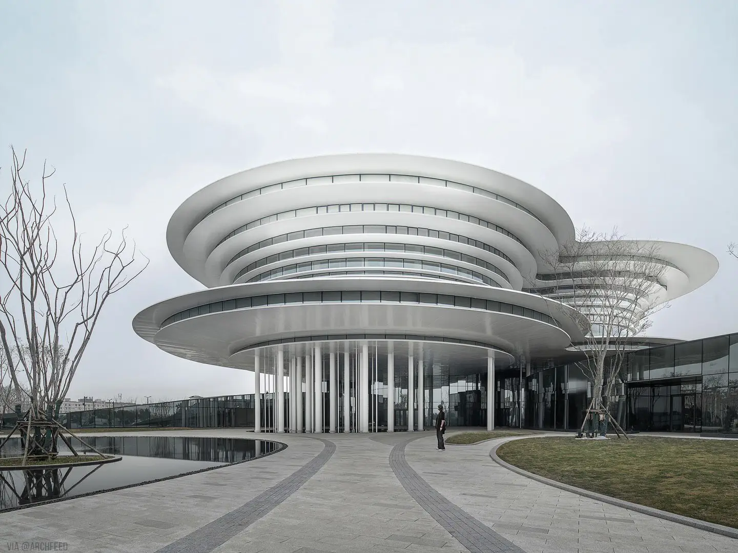 نمای ساختمان مدرن و معلق مرکز نمایشگاهی ابر فرودگاه چنگدو با طراحی سفید و کشیده بر فراز فضای سبز که نشان‌دهنده سبک معماری انتزاعی شرکت CSWADI است.