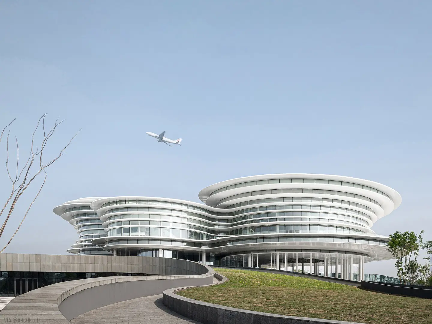 نمای ساختمان مدرن و معلق مرکز نمایشگاهی ابر فرودگاه چنگدو با طراحی سفید و کشیده بر فراز فضای سبز که نشان‌دهنده سبک معماری انتزاعی شرکت CSWADI است.
