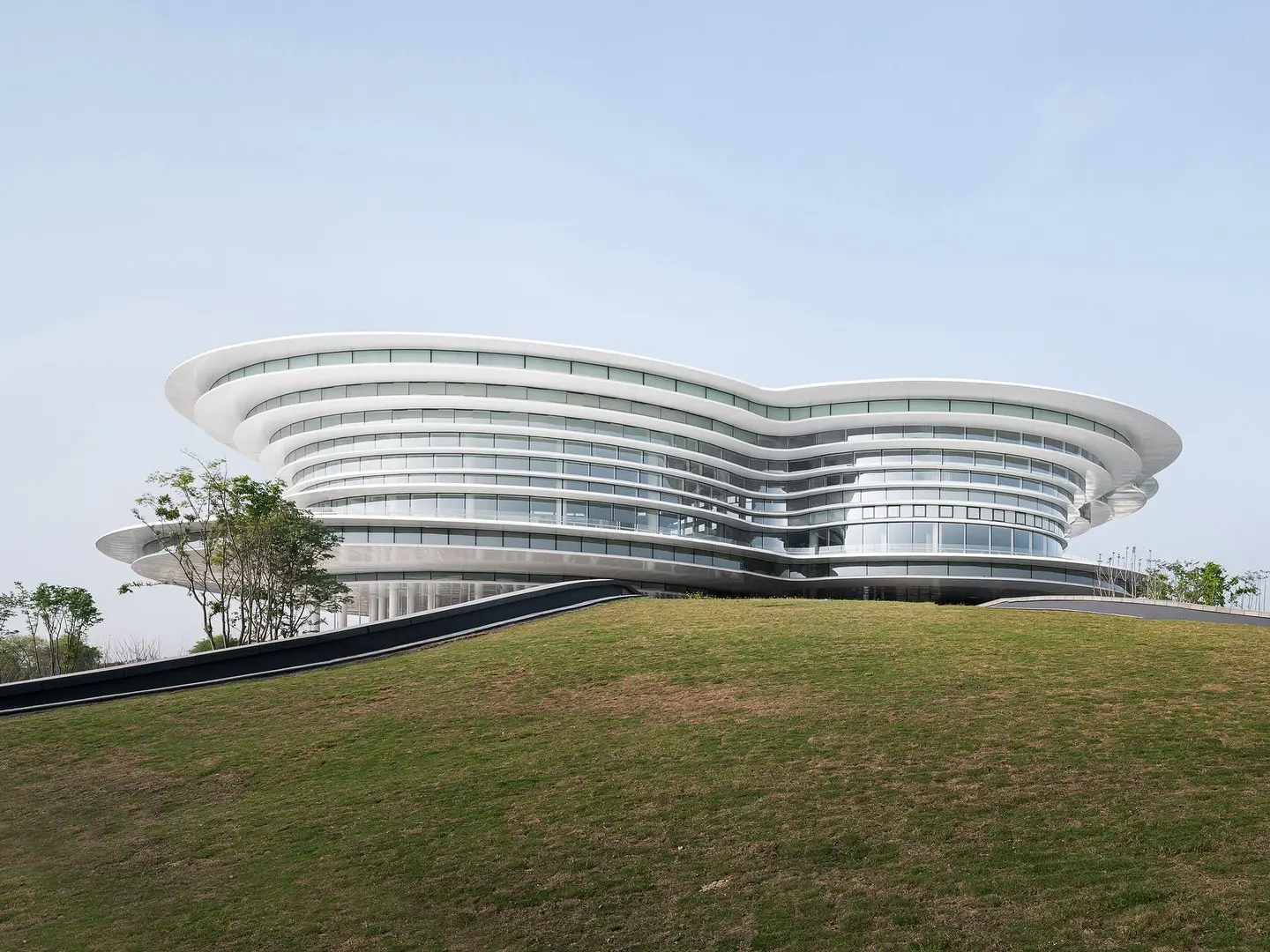 نمای ساختمان مدرن و معلق مرکز نمایشگاهی ابر فرودگاه چنگدو با طراحی سفید و کشیده بر فراز فضای سبز که نشان‌دهنده سبک معماری انتزاعی شرکت CSWADI است.