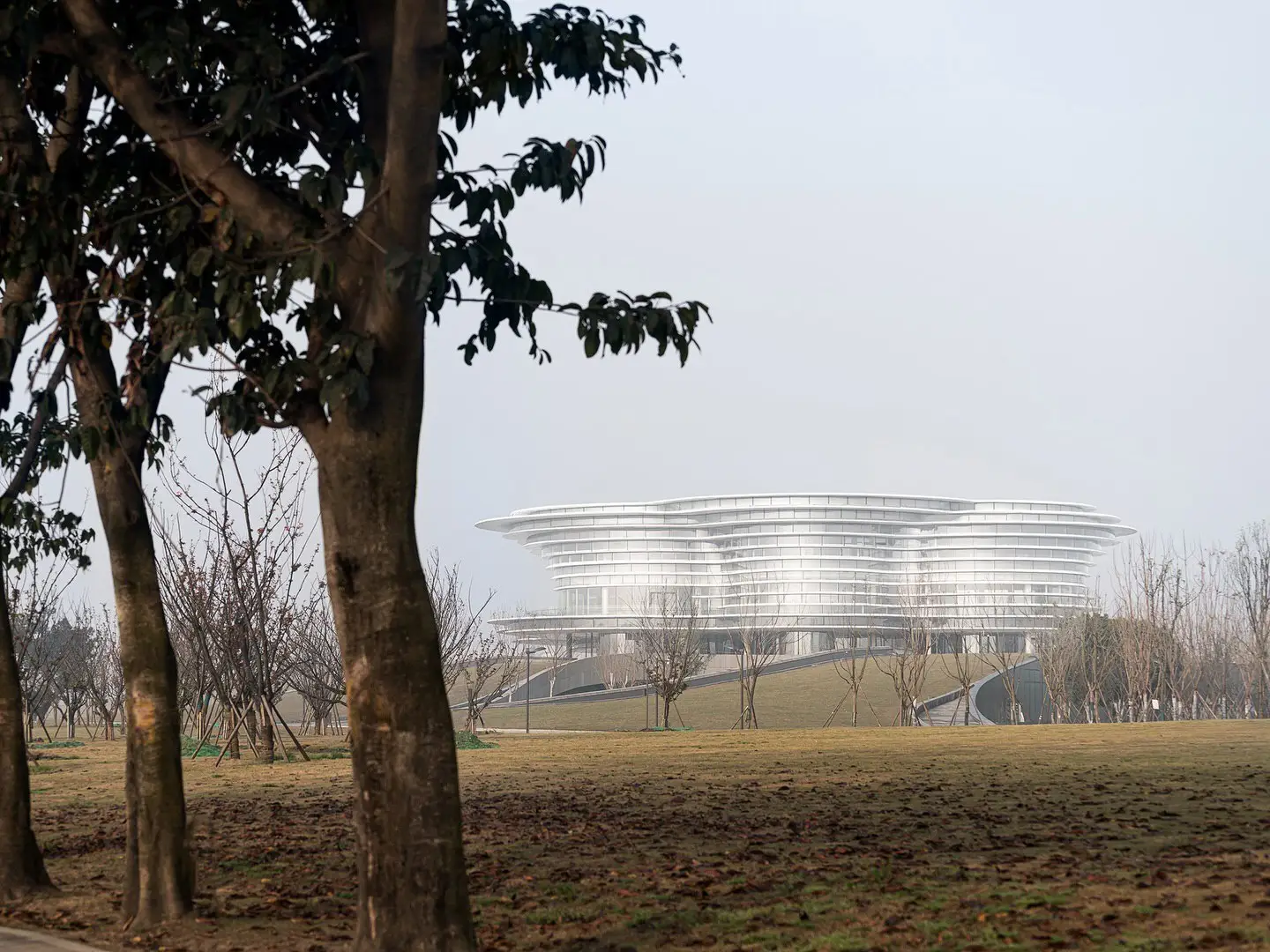 نمای ساختمان مدرن و معلق مرکز نمایشگاهی ابر فرودگاه چنگدو با طراحی سفید و کشیده بر فراز فضای سبز که نشان‌دهنده سبک معماری انتزاعی شرکت CSWADI است.