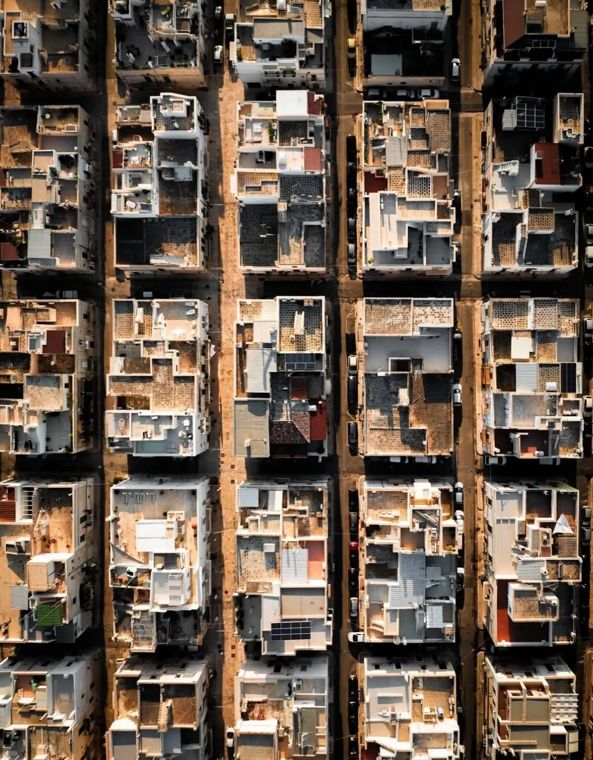 نمای هوایی عمودی از خانه‌های سفید با سقف‌های مسطح در شهر ساحلی پولینیانو آ ماره ایتالیا که در لبه صخره‌های مرتفع کنار دریای آبی قرار گرفته‌اند.