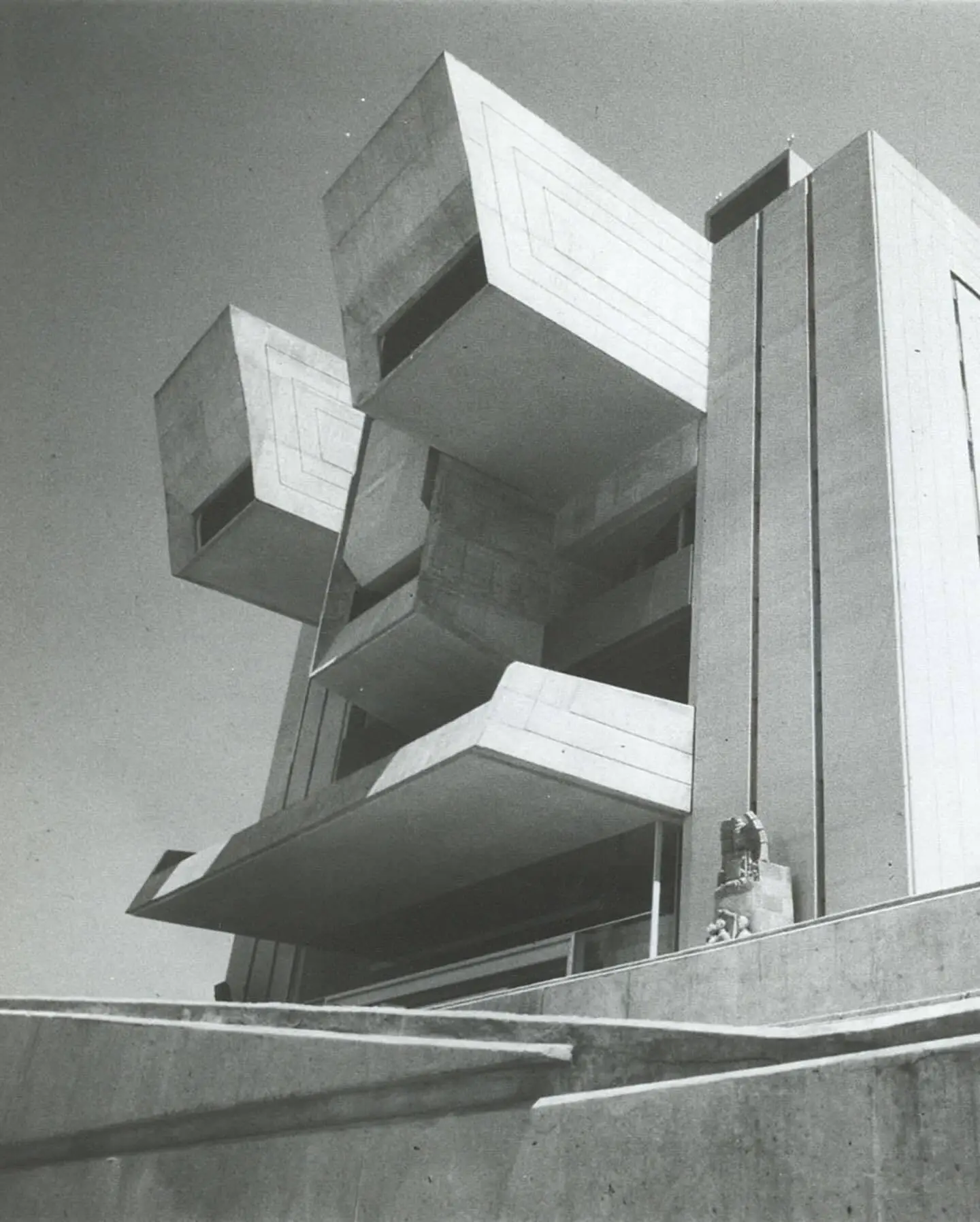 نمای ساختمان‌های بتنی به سبک بروتالیسم در مکزیک با هندسه صلب و سایه‌های عمیق که نشان‌دهنده ترکیب معماری مدرن و سنتی است.